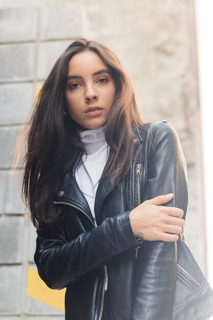 Retrato de una mujer joven hermosa en la chaqueta de cuero negra que mira la cámara