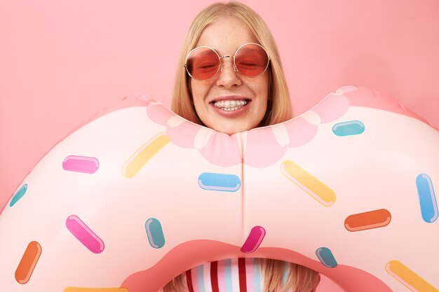 Retrato de mujer joven hermosa feliz con piercing facial sonriendo ampliamente, mostrando frenillos en sus dientes, con mirada despreocupada, relajándose en la piscina en un día soleado