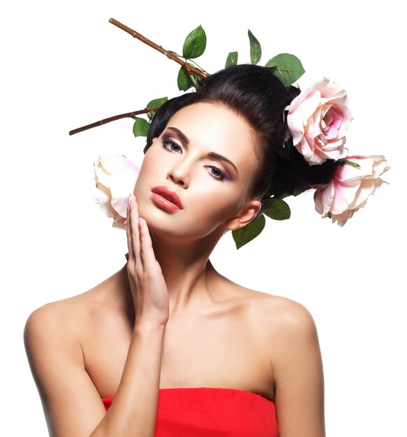 Retrato de mujer joven hermosa con flores en el pelo tocando su rostro - aislado en blanco