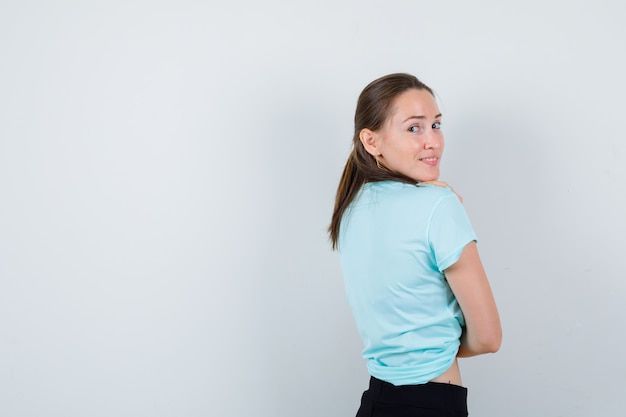 Retrato de mujer joven hermosa mirando por encima del hombro en camiseta y mirando alegre