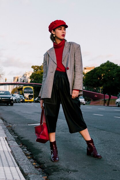 Retrato de una mujer joven hermosa que se coloca en el camino con el bolso