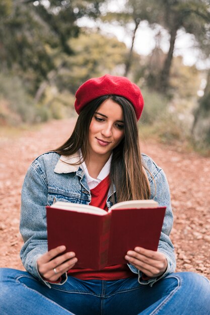 Retrato de una mujer joven hermosa que lee el libro en al aire libre