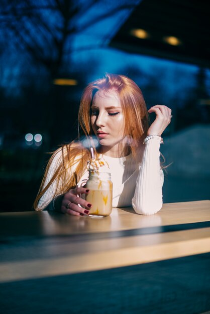 Retrato de una mujer joven hermosa que se sienta en café con el tarro del smoothie