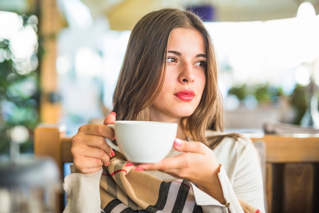 Retrato de una mujer joven hermosa que sostiene la taza de cerámica blanca