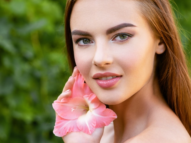 Retrato de mujer joven hermosa con rostro limpio. Hermoso rostro de mujer adulta joven con piel limpia y fresca - naturaleza. Rostro de la joven y bella mujer sexy al aire libre. Rostro de belleza con flor.