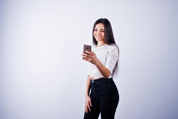 Retrato de una mujer joven y hermosa con top blanco y pantalones negros usando su teléfono