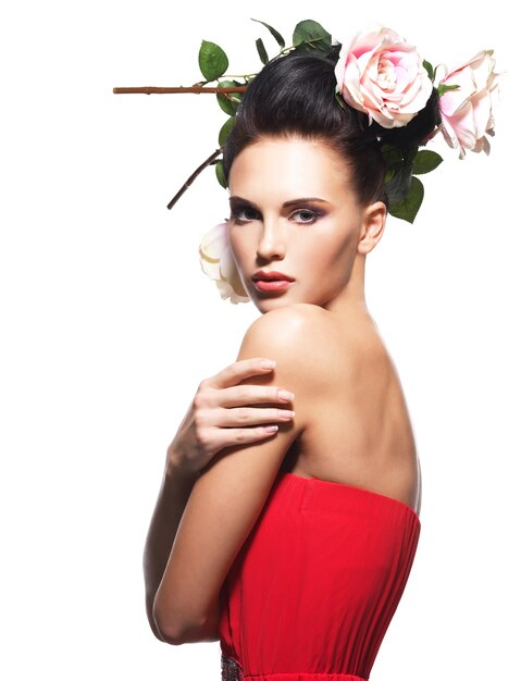 Retrato de mujer joven hermosa en un vestido rojo con flores en el pelo - aislado en blanco