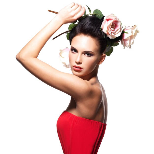 Retrato de mujer joven hermosa en un vestido rojo con flores en el pelo - aislado en blanco