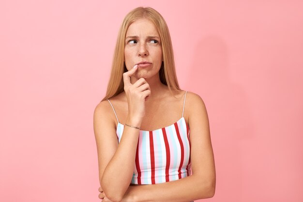 Retrato de mujer joven indecisa dudosa con pecas tocando los labios y mirando hacia otro lado, enfrentando el dilema, tomando decisiones, eligiendo qué ponerse para la fiesta