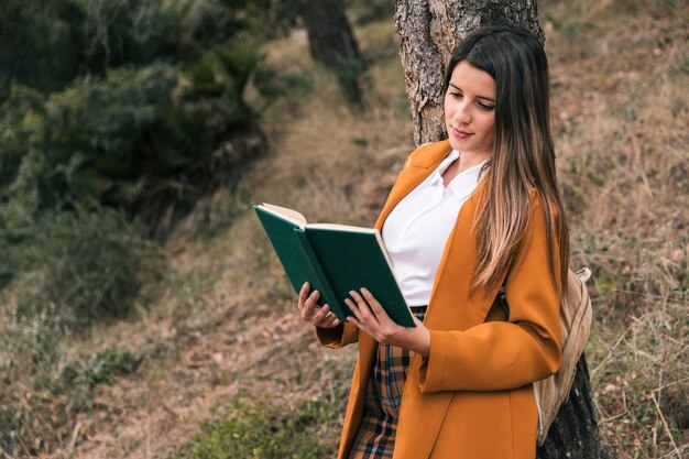 Retrato de una mujer joven leyendo el libro bajo el árbol