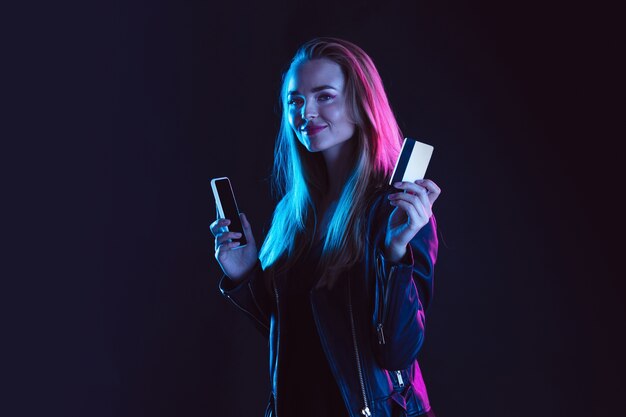 Retrato de mujer joven en luz de neón sobre fondo oscuro. Las emociones humanas, viernes negro, lunes cibernético, compras, ventas, concepto de finanzas.