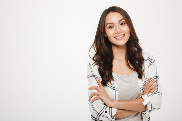 Retrato de mujer joven con magnífica sonrisa de pie con los brazos cruzados aislado, sobre blanco