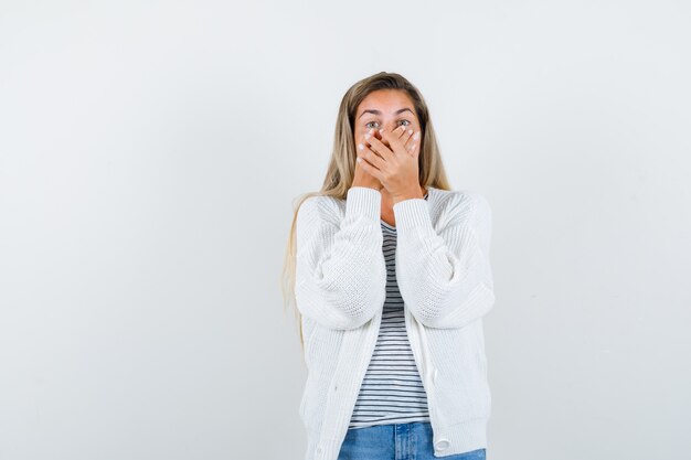 Retrato de mujer joven manteniendo las manos en la boca en camiseta, chaqueta y mirando asustado vista frontal