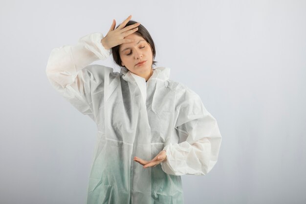 Retrato de mujer joven médico científico en bata de laboratorio defensiva comprobando la temperatura.