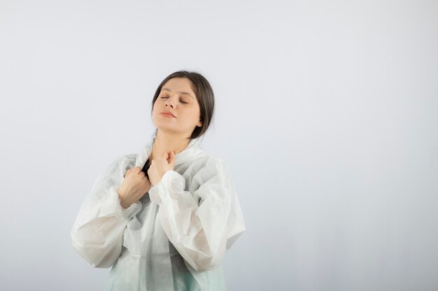 Retrato de mujer joven médico científico en bata de laboratorio defensiva tocando su garganta.