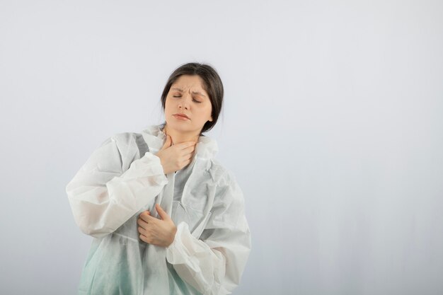 Retrato de mujer joven médico científico en bata de laboratorio defensiva tocando su garganta.