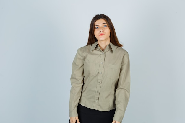 Retrato de mujer joven mirando a la cámara mientras curva los labios en camisa, falda y mirando perplejo vista frontal