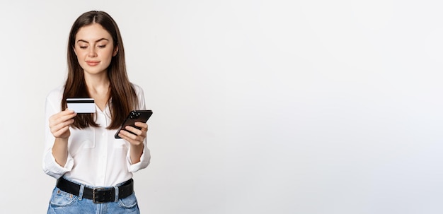 Foto gratuita retrato de mujer joven mirando la pantalla del teléfono inteligente pagando la compra en línea con tarjeta de crédito sta