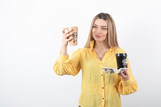 Retrato de mujer joven mirando tazas de café en la pared blanca.