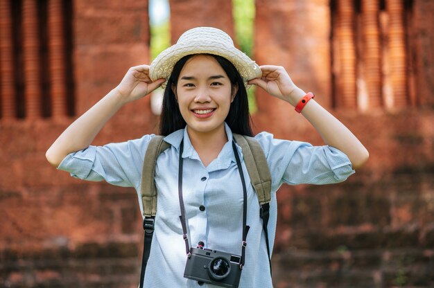 Retrato mujer joven mochilero con sombrero viajando en un sitio antiguo, ella sonriendo y mirando a la cámara con felicidad, espacio de copia