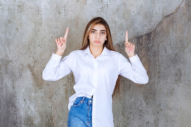 Retrato de mujer joven modelo de pie y apuntando sobre mármol