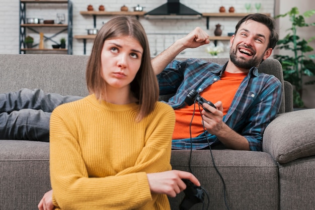 Retrato de mujer joven molesta sentada cerca del joven sonriente que anima mientras juega el videojuego
