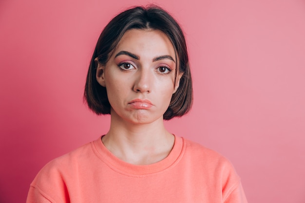 Retrato de mujer joven molesta triste con maquillaje brillante sobre fondo rosa