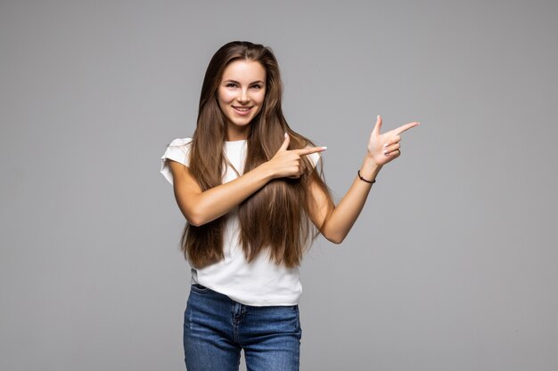 Retrato de mujer joven mostrando apuntando hacia arriba y hacia el lado con los dedos, fondo gris aislado