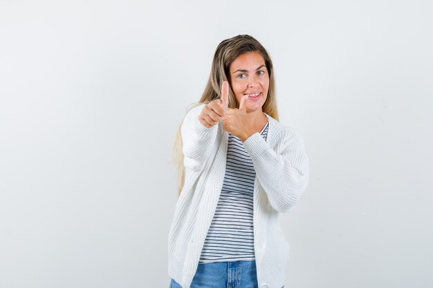 Retrato de mujer joven mostrando doble pulgar hacia arriba en camiseta, chaqueta y mirando feliz vista frontal