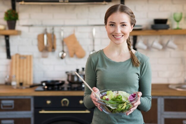 Retrato de mujer joven mostrando ensalada recién hecha