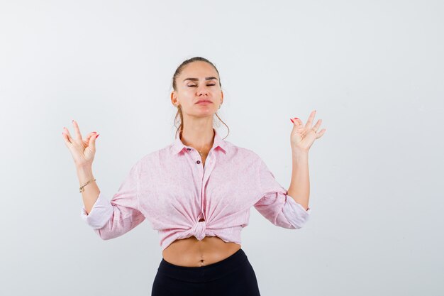 Retrato de mujer joven mostrando gesto de meditación en camisa casual y mirando pacífica vista frontal