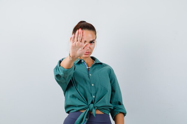 Retrato de mujer joven mostrando gesto de parada en camisa verde y mirando molesto vista frontal