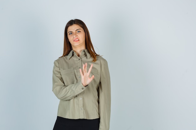 Retrato de mujer joven mostrando gesto de parada, frunciendo el ceño con disgusto en camisa, falda y mirando disgustado vista frontal