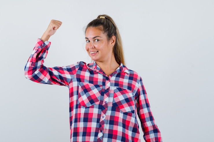 Foto gratuito retrato de mujer joven mostrando los músculos del brazo en camisa casual y mirando orgullosa vista frontal