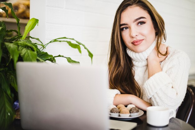 Retrato de una mujer joven con ordenador portátil; Trufas de café y chocolate en mesa