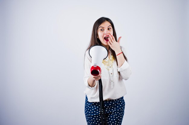 Retrato de una mujer joven con pantalones azules y blusa blanca posando con megáfono en el estudio