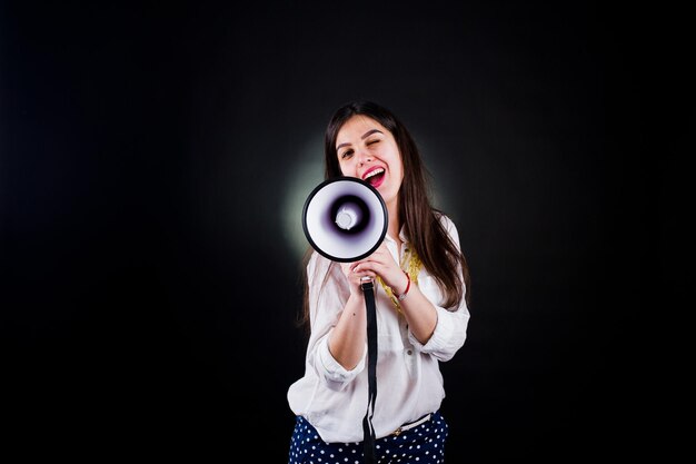 Retrato de una mujer joven con pantalones azules y blusa blanca posando con megáfono en el estudio