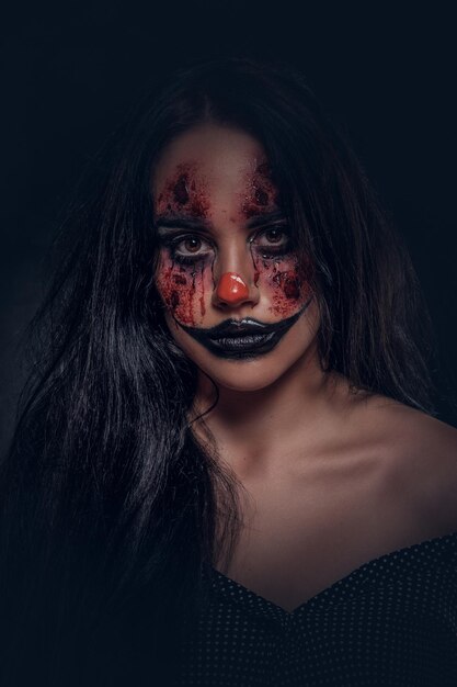 Retrato de mujer joven en un papel de payaso malvado y aterrador en un estudio fotográfico oscuro.