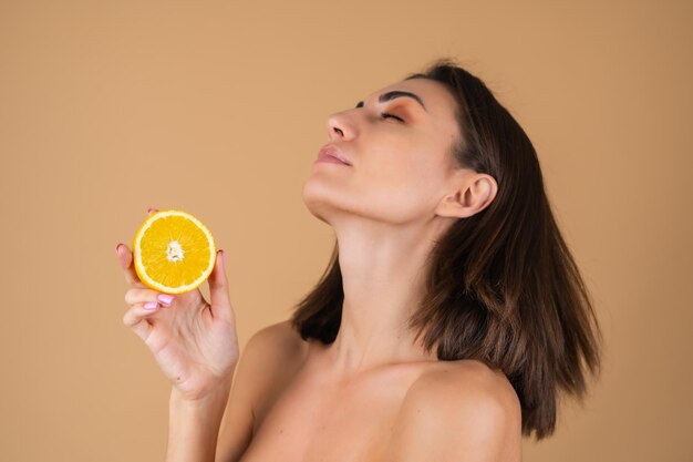 Retrato de una mujer joven en una pared beige con maquillaje cálido natural y piel suave y limpia, sosteniendo círculos naranjas