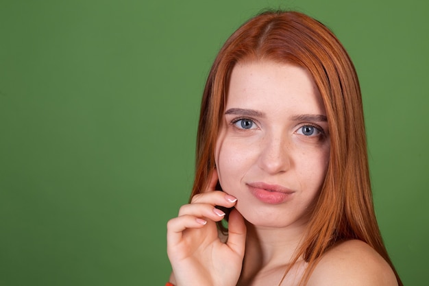 Retrato de mujer joven de pelo bastante rojo con suave piel suave natural con hombros desnudos en la pared verde, concepto de belleza