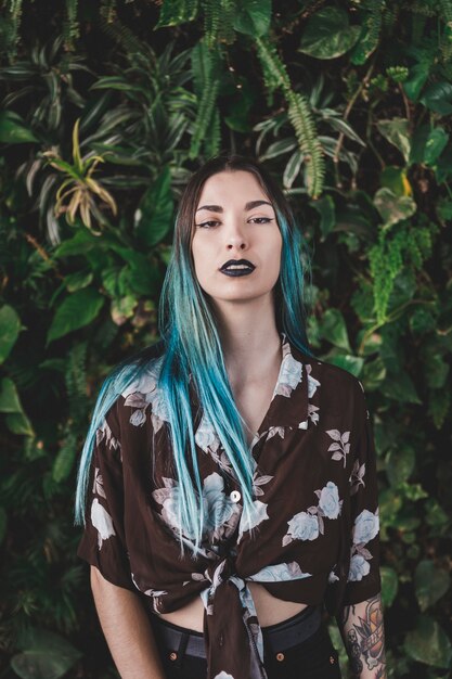 Retrato de una mujer joven con el pelo teñido de pie delante de la planta