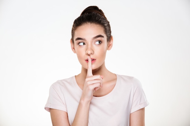 Retrato de mujer joven pensativa hermosa con piel perfecta sosteniendo el dedo índice en los labios pidiendo guardar silencio o secreto