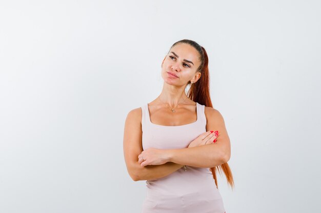 Retrato de mujer joven de pie con los brazos cruzados en la parte superior del tanque blanco y mirando confiada vista frontal