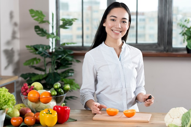 Retrato de una mujer joven de pie cerca del mostrador de la cocina con diferentes tipos de verduras y frutas