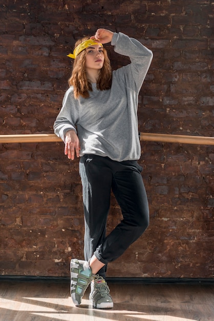 Foto gratuita retrato de una mujer joven de pie contra la pared de ladrillo que se inclina en la barra