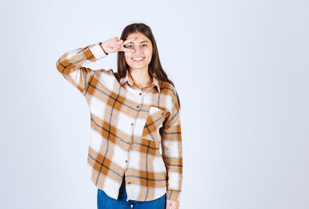 Retrato de mujer joven de pie y sonriendo a la cámara sobre una pared blanca.