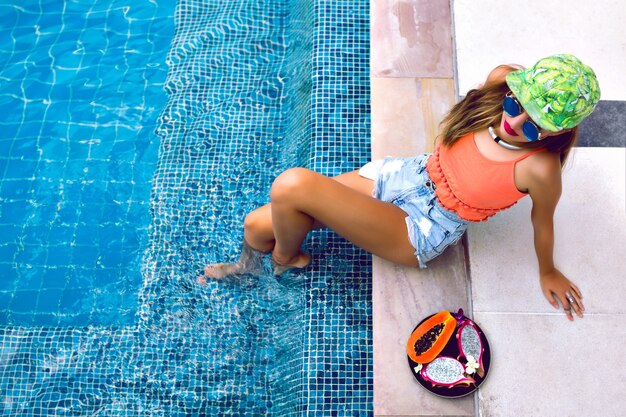 Retrato de mujer joven posando junto a la piscina con frutas tropicales