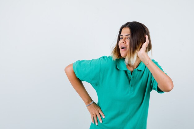 Retrato de mujer joven posando mientras mantiene la mano en la cabeza en la camiseta de polo y mirando alegre vista frontal