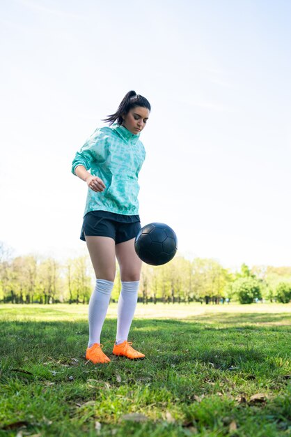 Retrato de mujer joven practicando habilidades futbolísticas y haciendo trucos con la pelota de fútbol