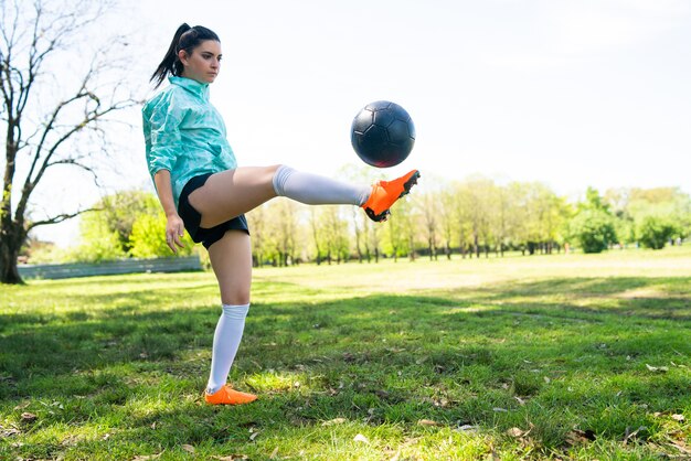 Retrato de mujer joven practicando habilidades futbolísticas y haciendo trucos con la pelota de fútbol